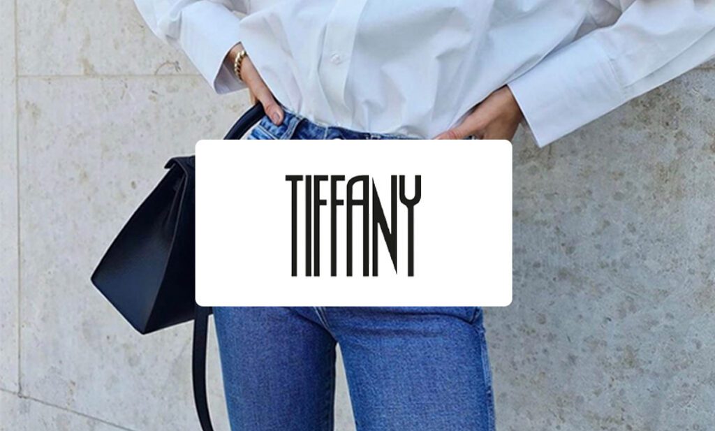 Tiffanys hvide logo i forgrunden med en kvinde iført hvid skjorte og blå jeans i baggrunden.