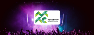 Koncertoplevelse med lilla scenelys hos Aalborg Kongres & Kultur Center (AKKC), med AKKC’s logo i hvidt i billedets forgrund.