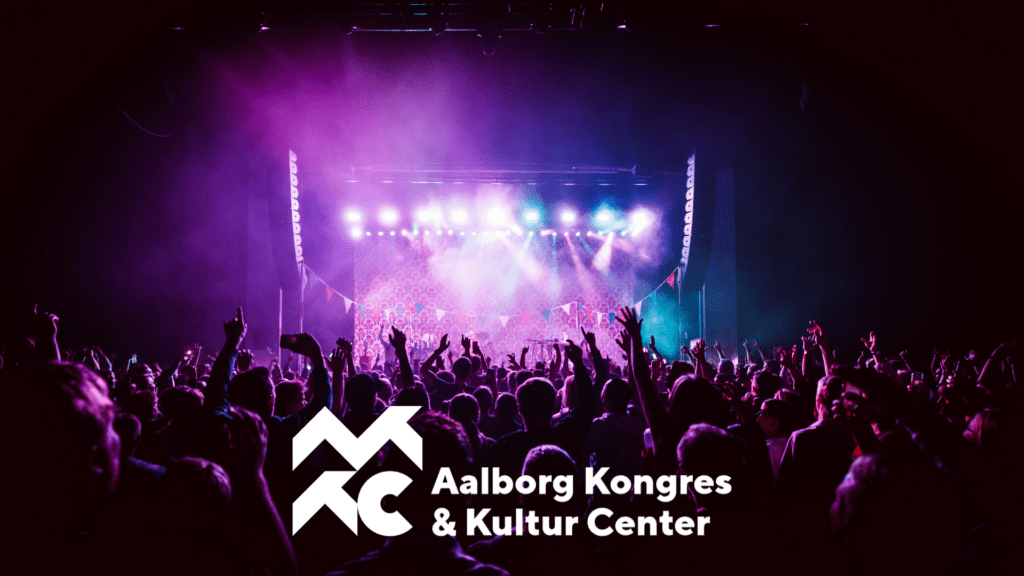 Koncertoplevelse med lilla scenelys hos Aalborg Kongres & Kultur Center (AKKC), med AKKC’s logo i hvidt i billedets forgrund.