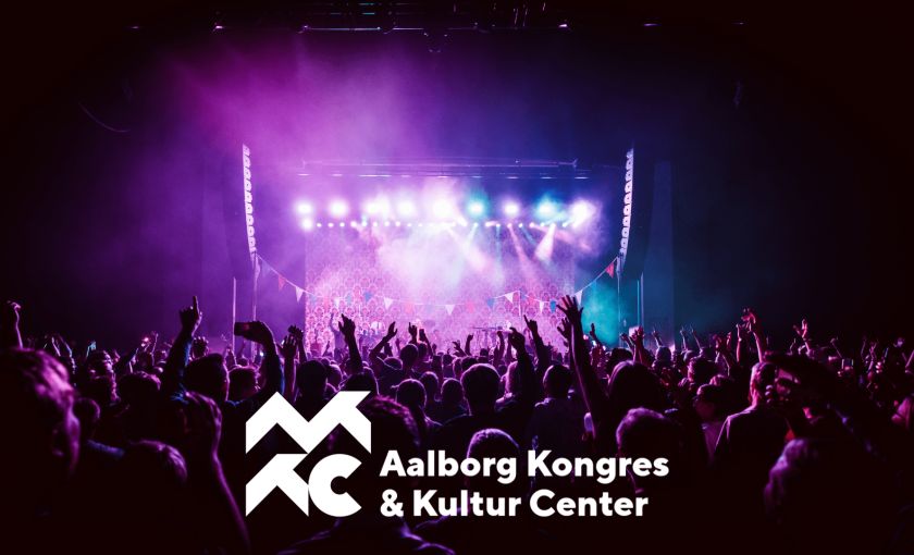 Koncertoplevelse med lilla scenelys hos Aalborg Kongres & Kultur Center (AKKC), med AKKC’s logo i hvidt i billedets forgrund.