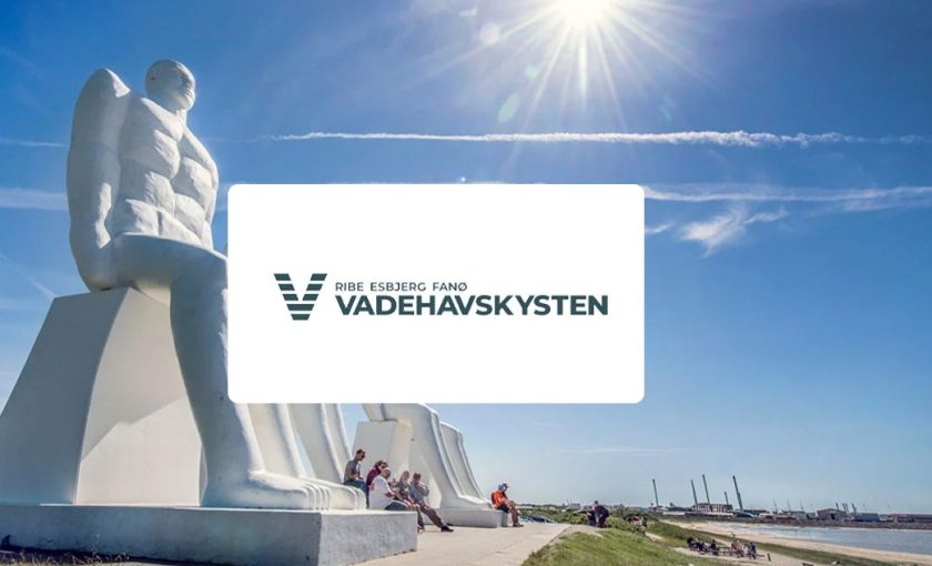 Mennesket ved Havet skulpturer i Esbjerg under solrig himmel, med Vadehavskystens logo.